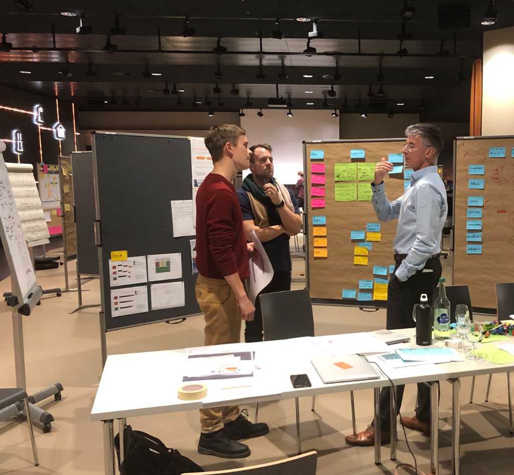 Anthony Smith im Gespräch mit zwei Teilnehmenden eines Workshops vor Pinnwänden voller Haftnotizen