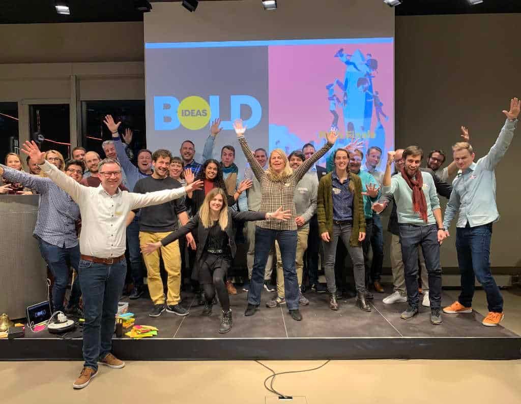 Anthony Smith mit einer grossen Gruppe auf einer Bühne nach einem Design-Thinking-Sprint, alle mit erhobenen Armen, auf der Leinwand der Schriftzug «BOLD Ideas»
