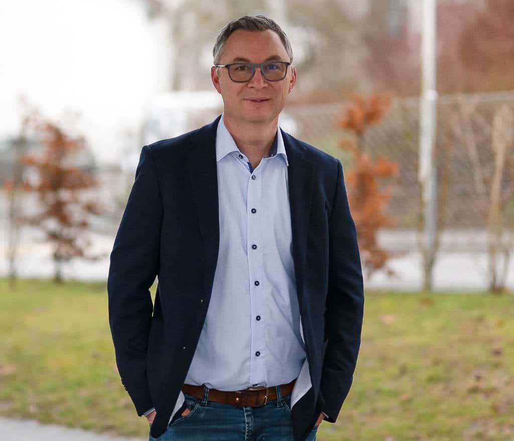 Anthony Smith in Sakko und Hemd im Freien, die Hände in den Hosentaschen